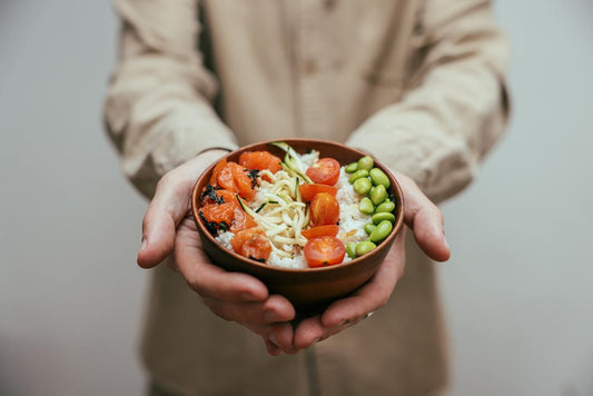 A person holding a bowl of rice with chopped tomatoes
